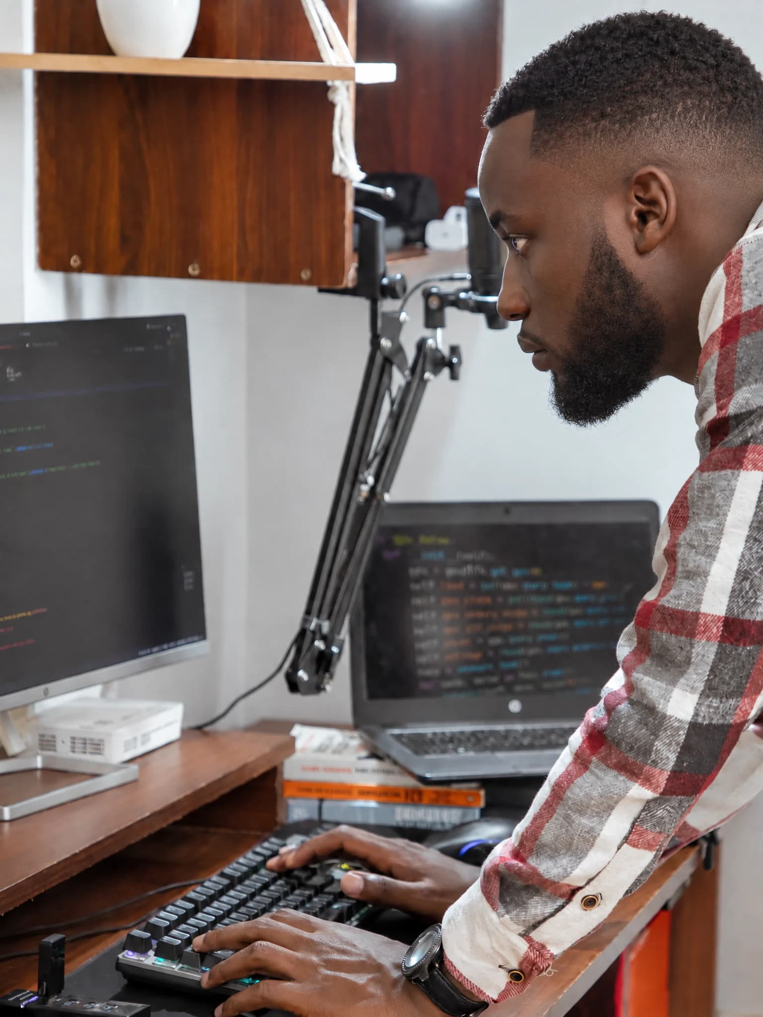 Man leaning over a keyboard beside screens displaying code